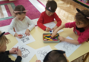 Dzieci siedzą przy stoliku, kolorują ilustracje kotów z różnych znanych bajek